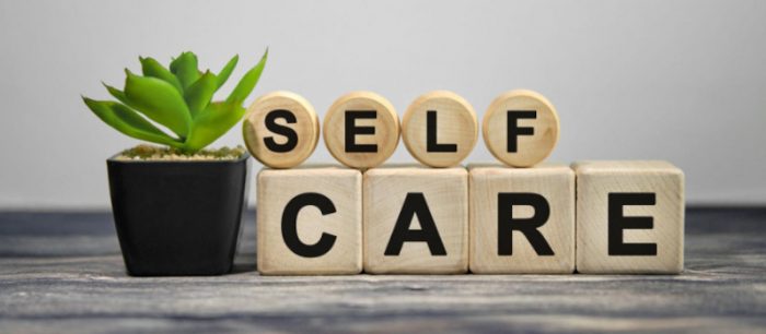 Practice Self Care - small potted plant next to the words Self Care in blocks on a wooden table